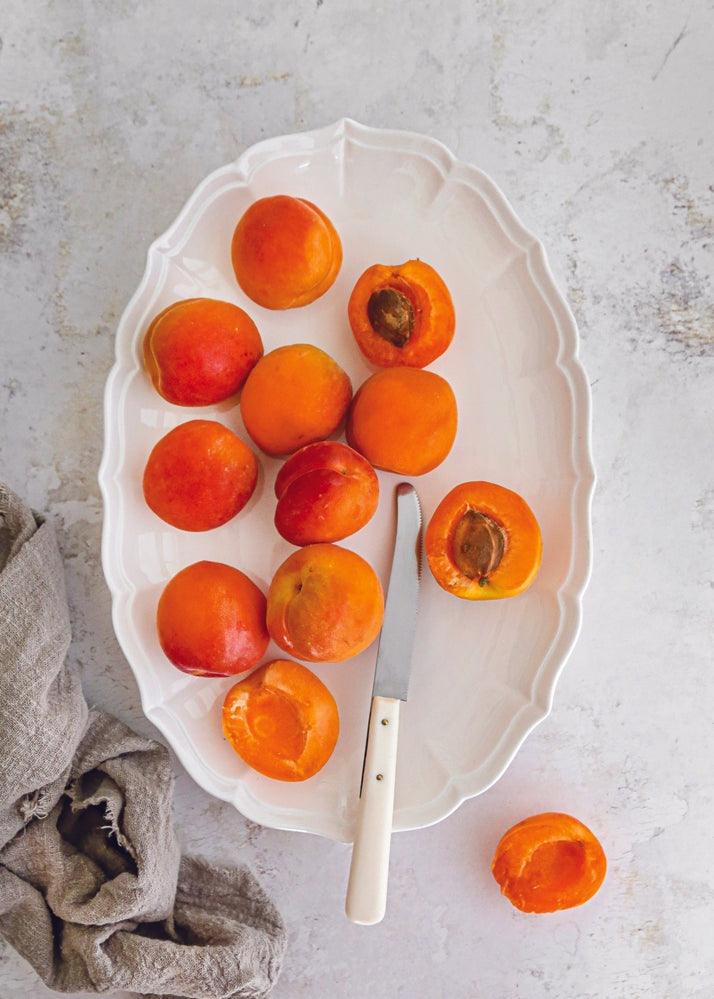 PAPAIA still life con albicocche su piatto bianco con coltello e stoffa in cotone